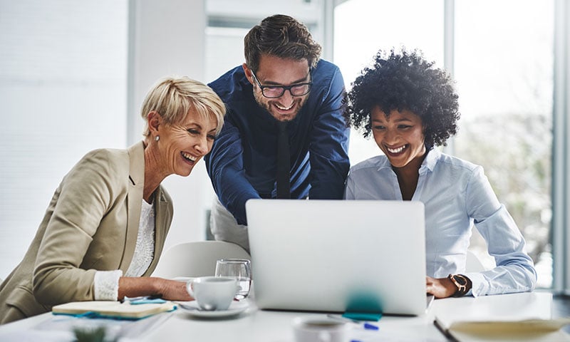 Two women and a man around a laptop in a conference room 